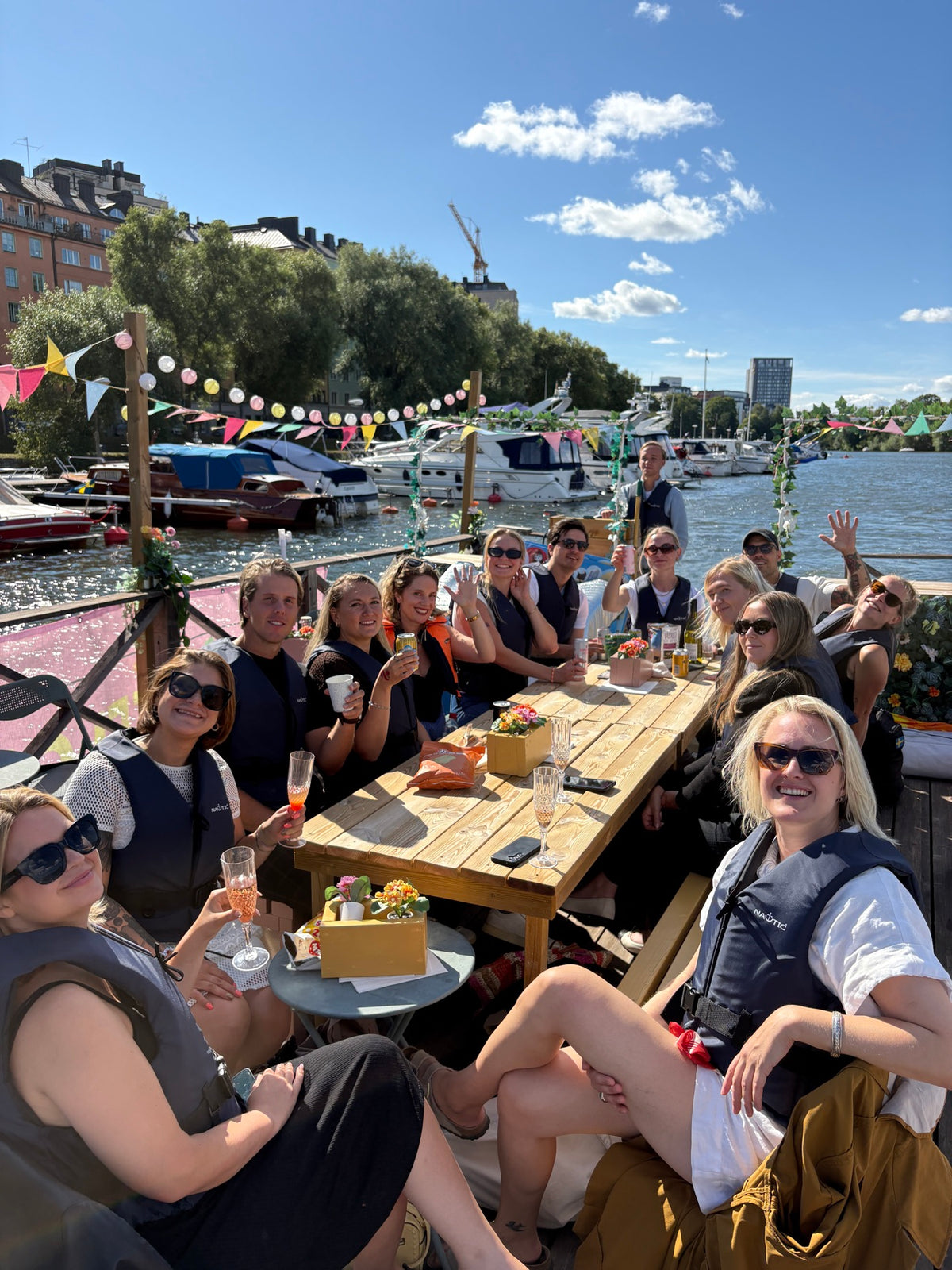 Fullsatt sällskap i flötvästar vid bordet på Festflotten medan den kryssar förbi båtar och hus i Stockholm